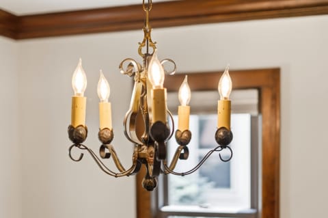 A brass chandelier with six candle-like bulbs hanging from the ceiling, illuminating a cozy room with wooden accents.