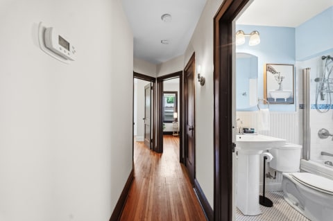 A well-lit hallway with hardwood floors and dark wood trim, featuring a bathroom at the end.