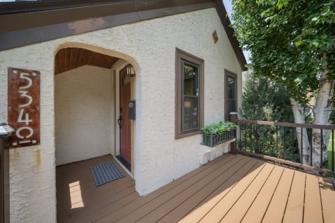 Charming entrance with arched doorway, wooden deck, and lush plants.