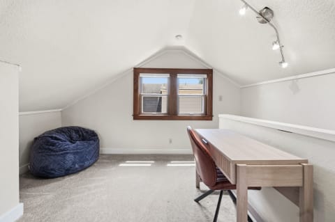 A serene attic workspace with vaulted ceilings, a wooden desk, brown chair, and navy blue bean bag.