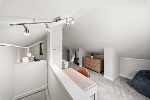 A bright upstairs loft with a desk, leather chair, dresser, and beanbag chair under a sloped ceiling.