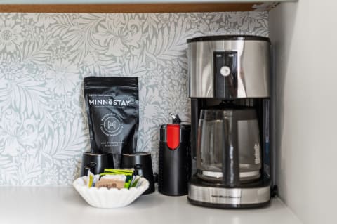 A modern coffee maker, black coffee beans bag, two coffee cups, and assorted condiments on display.