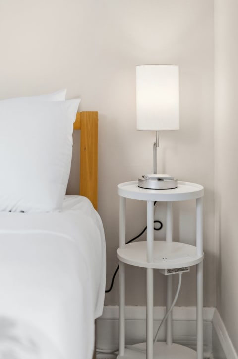 A cozy bedside corner with a white lamp, crisp linens, and a minimalist table.
