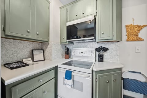 A kitchen with sage-green cabinets, white countertops, and modern appliances, showcasing a warm and inviting atmosphere.
