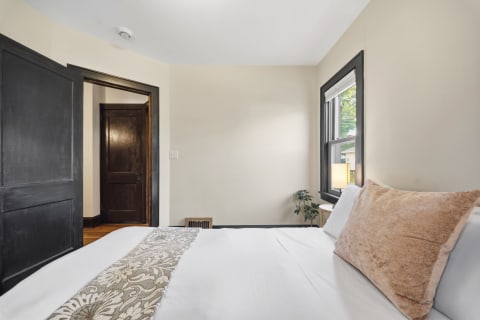 A cozy bedroom with a plush bed, decorative pillow, and natural light from the window, creating a peaceful atmosphere.