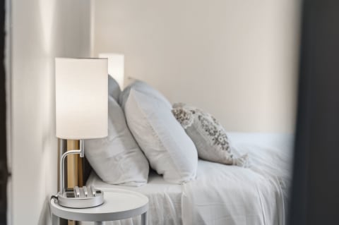 A cozy bedroom featuring soft white linens, fluffy pillows, and a stylish bedside lamp with a charging station.