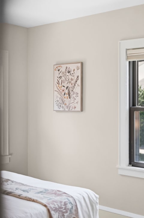 A tranquil bedroom corner featuring botanical wall art and a neatly made bed with light linens.