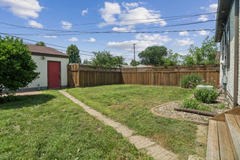 A spacious backyard with green grass, a red shed, and a wooden fence surrounded by plants and flowers.