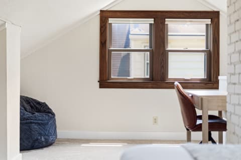 A cozy nook in a loft with a navy beanbag chair and a wooden desk under vaulted ceilings and bright windows.