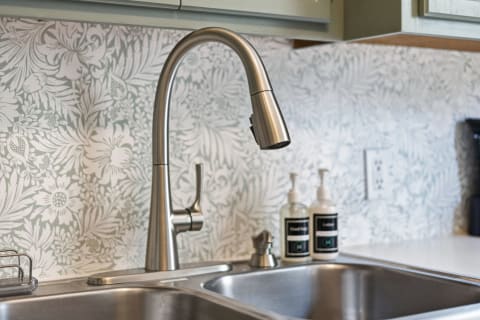 A stainless steel kitchen sink with a stylish faucet and a floral-patterned backsplash.