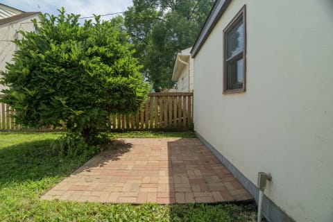 A peaceful outdoor space with a brick patio and a large leafy tree in a residential neighborhood.