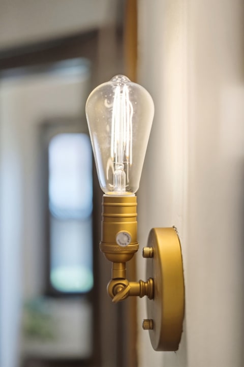 Golden brass Edison-style wall sconce with an exposed filament bulb illuminated in a softly lit hallway.