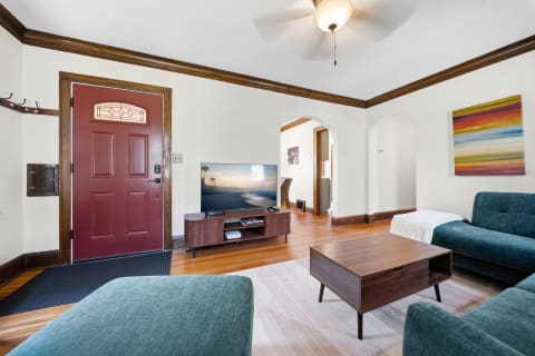A cozy living room with teal seating, wooden accents, and a flat-screen TV displaying a beach scene.
