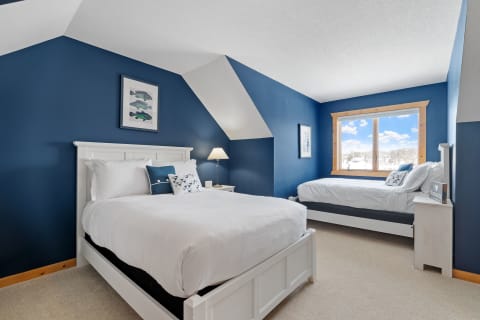 Interior of a bedroom with navy blue walls, a queen bed, and a daybed by the window.