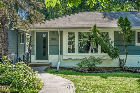 A charming single-story house with a green door, landscaped garden, and large windows.