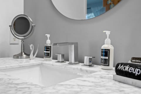 Modern bathroom sink with marble countertop, faucet, hand soap, lotion, and a makeup towel.