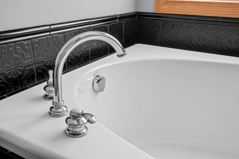 Close-up of a white bathtub with chrome faucet and black tiled wall.