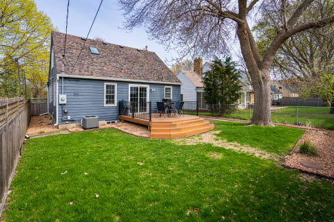 Backyard view featuring a blue house, wooden deck, and green lawn.