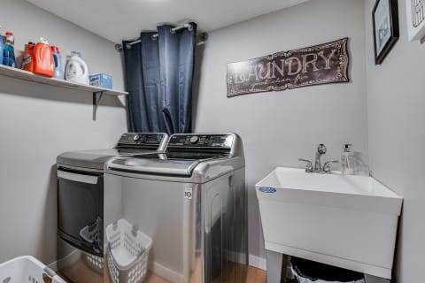 A laundry room featuring two washing machines, a laundry sink, and various cleaning products on a shelf.