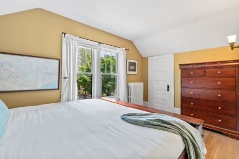 Warm bedroom with mustard walls, a map, and large windows overlooking greenery.