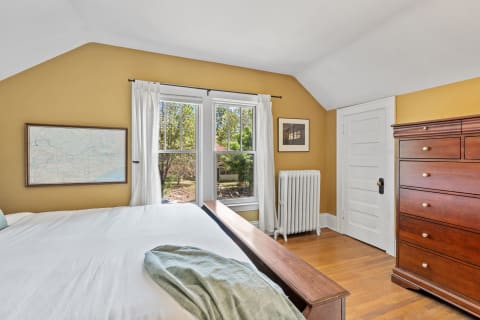 A bright bedroom featuring yellow walls, a wooden dresser, and a vintage map on the wall.