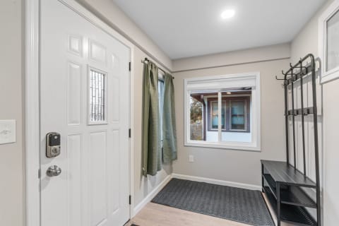 Entryway featuring a white door, coat rack, green curtains, and storage bench.