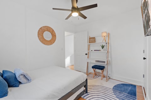Modern bedroom with a bed, blue pillows, a ceiling fan, and open shelving.