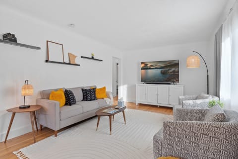 A contemporary living room featuring a light gray sofa, patterned chairs, and a TV cabinet.