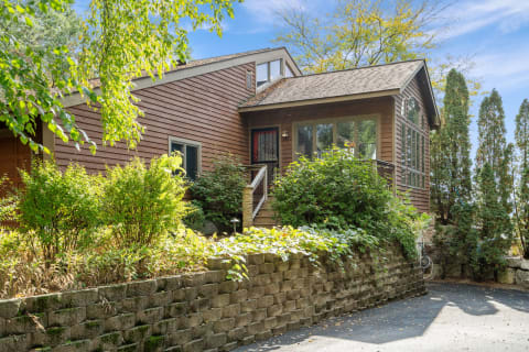 Modern wooden house surrounded by greenery and a stone wall.