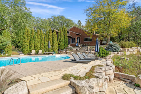 Outdoor swimming pool with lounge chairs and a wooden house surrounded by greenery.