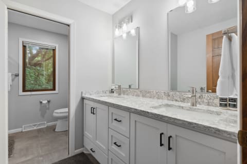 Modern bathroom with marble vanity, mirrors, and a window overlooking greenery.