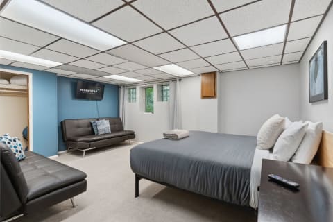A modern basement bedroom featuring a queen bed, a sofa bed, and a mounted TV.