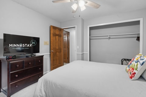 A well-decorated bedroom featuring a flat-screen TV, a dresser, and a spacious closet.
