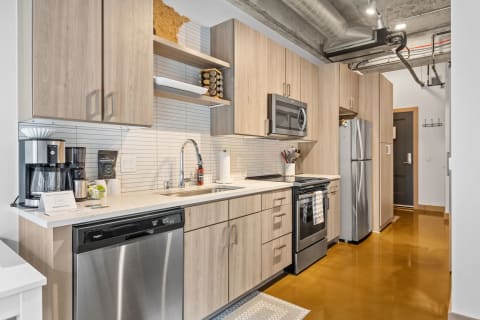 Modern kitchen featuring light wood cabinets, stainless steel appliances, and a polished amber floor.
