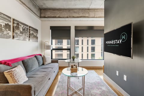 A contemporary living room featuring a gray sofa, glass coffee table, and city skyline art on the wall.