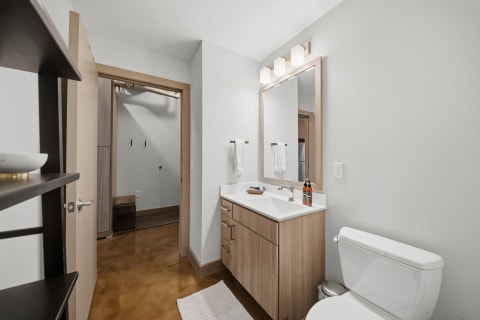 A contemporary bathroom featuring a wooden vanity, mirror, and polished concrete flooring.