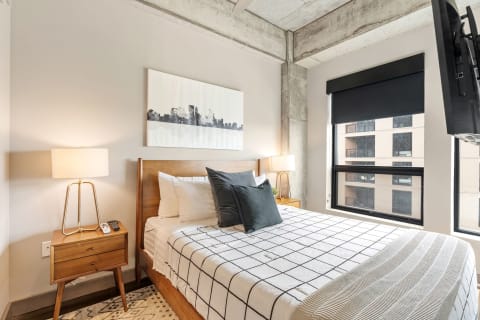 A stylish bedroom with a wooden bed, black grid patterned bedding, and modern decor.