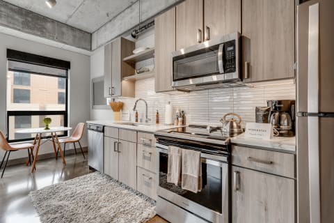 Modern kitchen featuring wood cabinets, stainless steel appliances, and a dining table by a window.