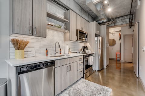 Modern kitchen with light wood cabinets, stainless steel appliances, and a fluffy rug.