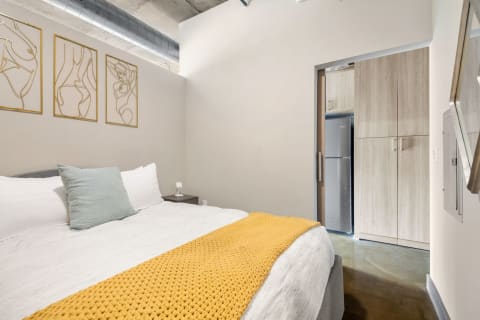 A modern bedroom featuring a bed with a mustard throw, abstract wall art, and a closet area.