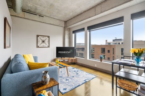 Modern living room featuring a couch, coffee table, and dining area with large windows.