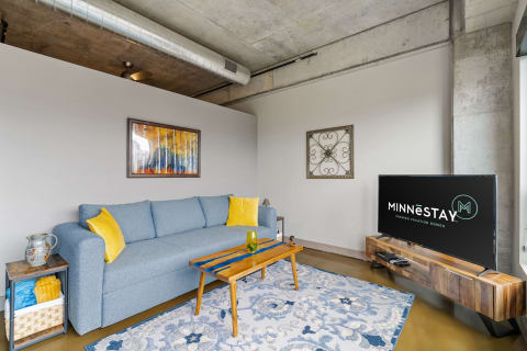 A modern living room featuring a blue couch, a wood coffee table, abstract artwork, and a television.