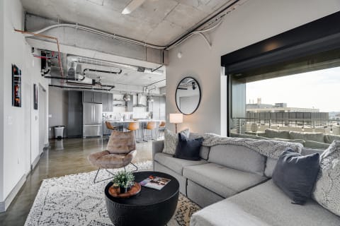 Stylish living room with gray sofa, round coffee table, and kitchen in the background.