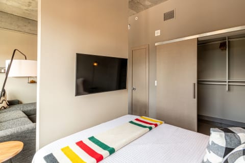 A contemporary bedroom featuring a bed with a colorful throw, a TV on the wall, and a gray couch.