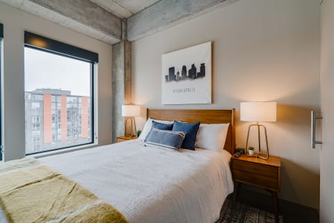 Contemporary bedroom featuring a queen bed, blue pillows, and a skyline artwork above.