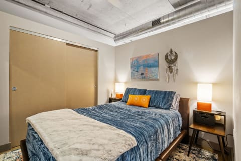 Cozy bedroom with a blue bedspread, decorative pillow, dreamcatcher, and tranquil wall art.