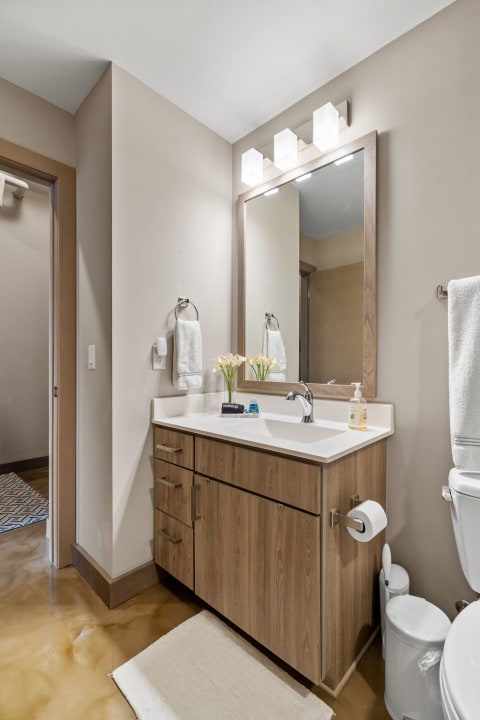 Modern bathroom with light wooden vanity, mirror, and yellow flowers.