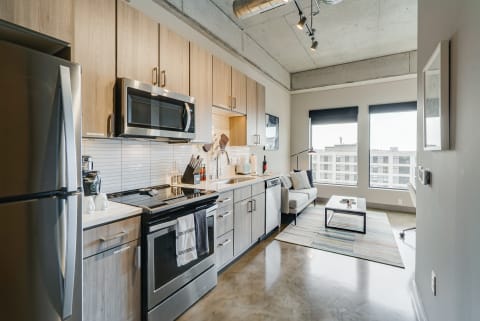 Modern kitchen with stainless steel appliances and a cozy living area featuring a gray sofa and coffee table.
