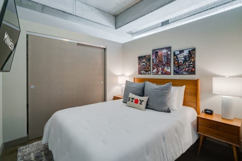 A modern bedroom with a wooden bed, decorative pillows, and vibrant cityscape artworks on the wall.