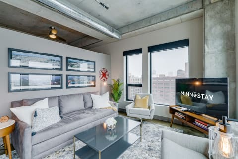 A contemporary living room with gray furniture, framed photographs, and a large window view.